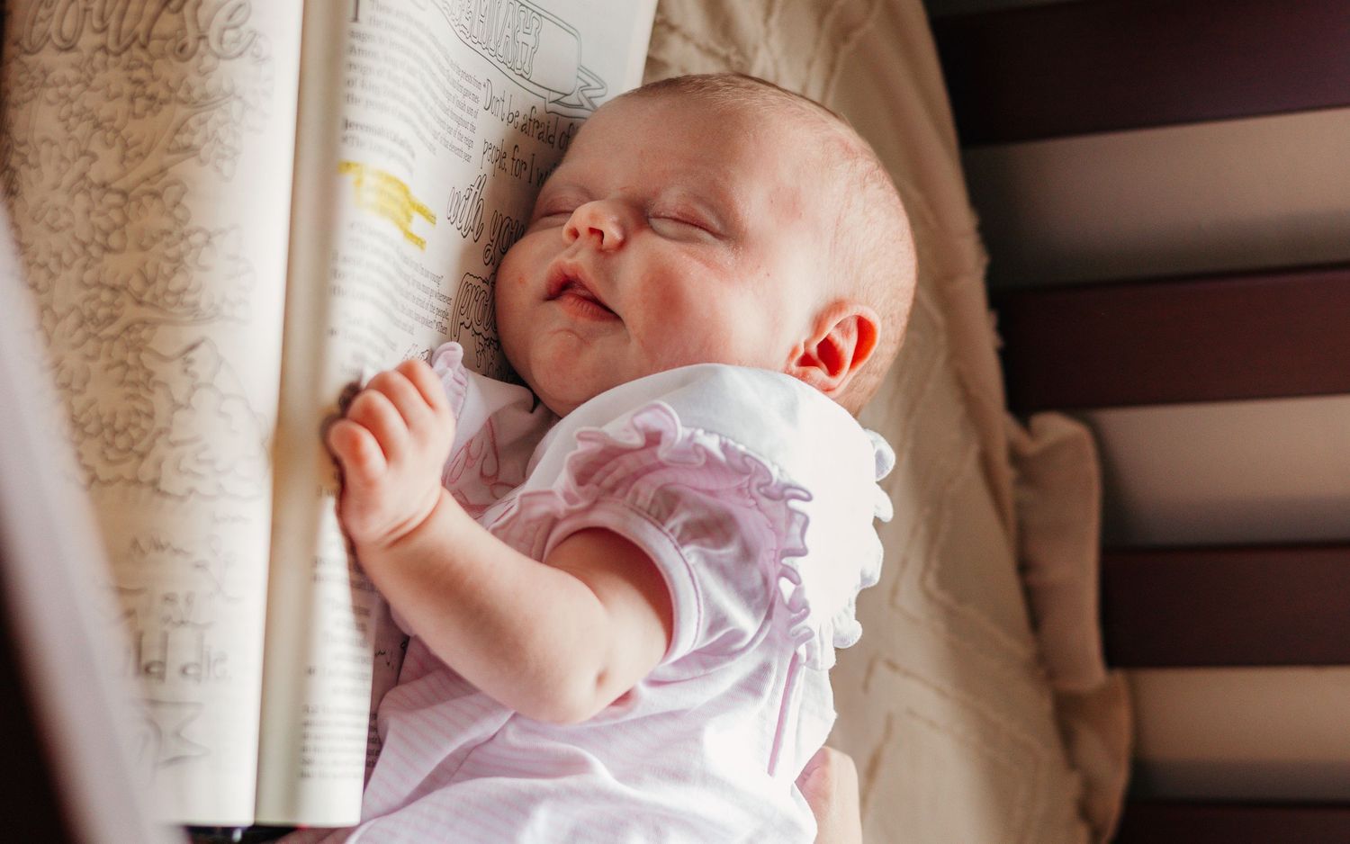 Sleeping newborn baby resting peacefully beside an open bible during a cozy newborn photography session.