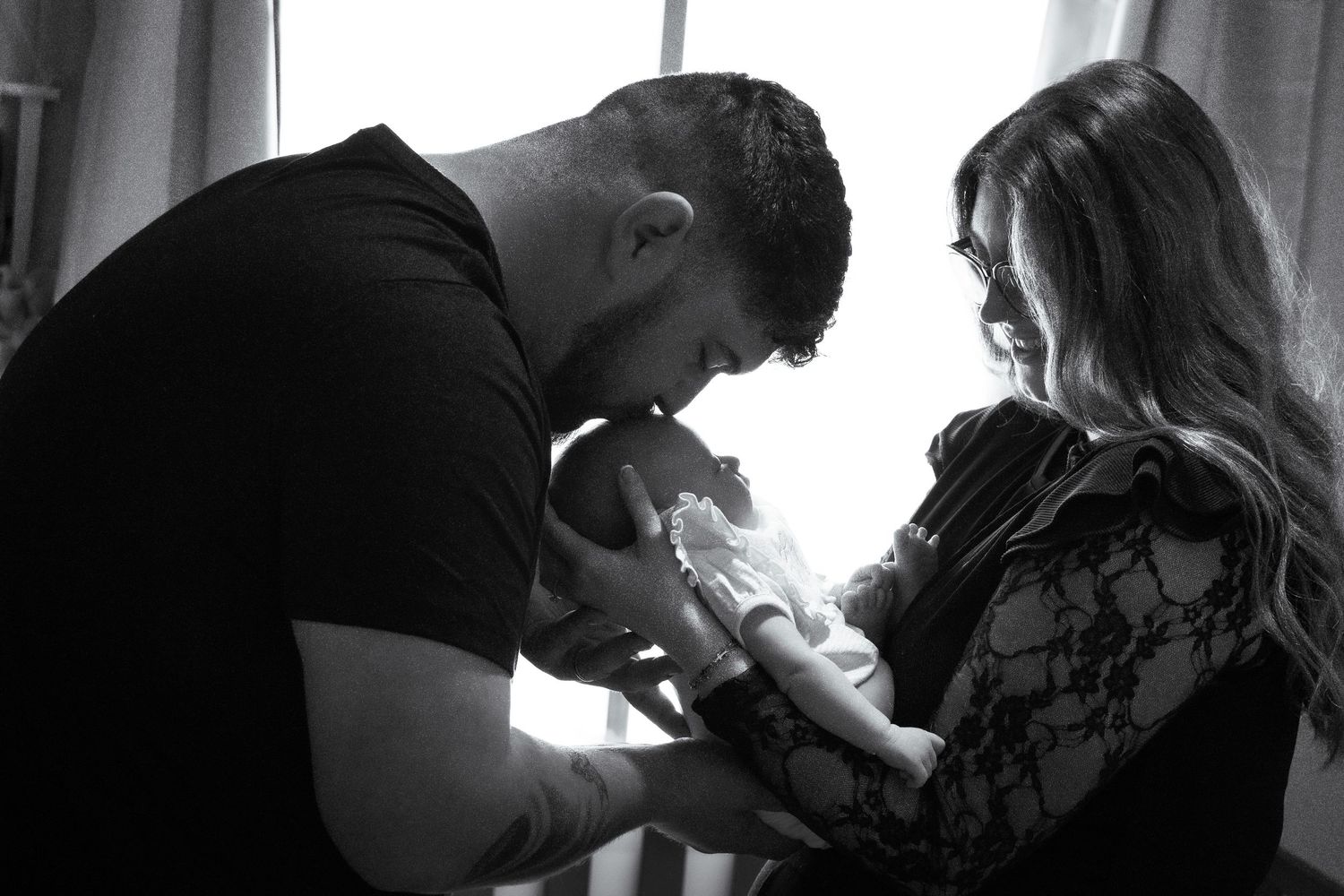 Parents gently holding their newborn baby together during an intimate lifestyle newborn photography session.