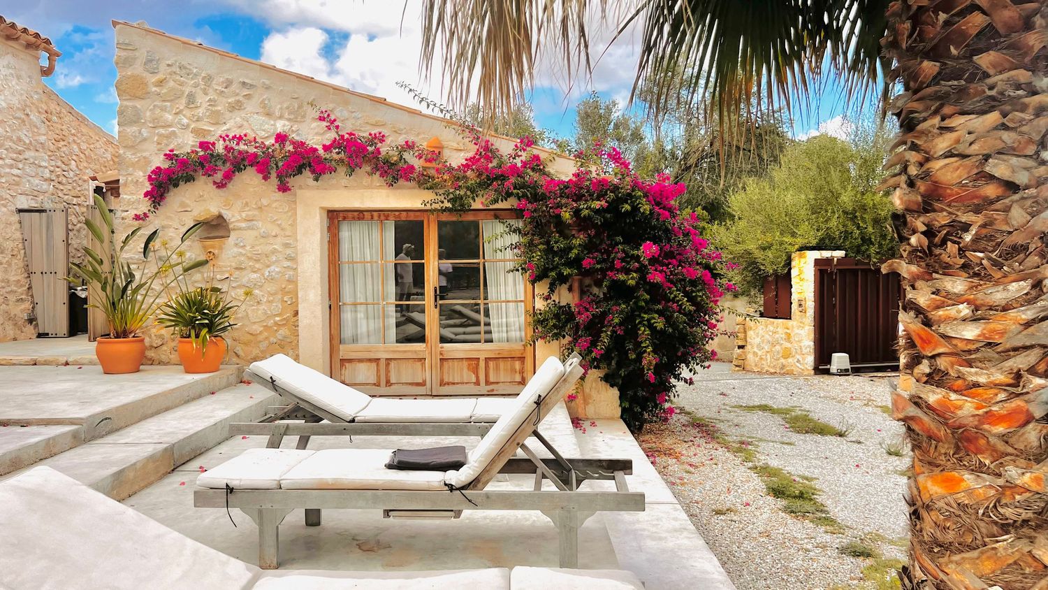 Panoramic view of a Mediterranean villa with pink bougainvillea flowers and wooden loungers on a sunny terrace.