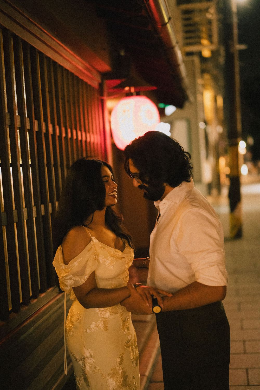 Couple sharing an intimate moment on a city sidewalk at night, glowing red sign in background.