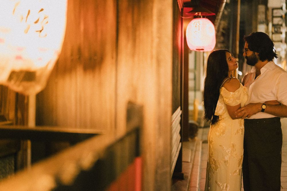 Couple embracing intimately beside a glowing red Japanese lantern at night.