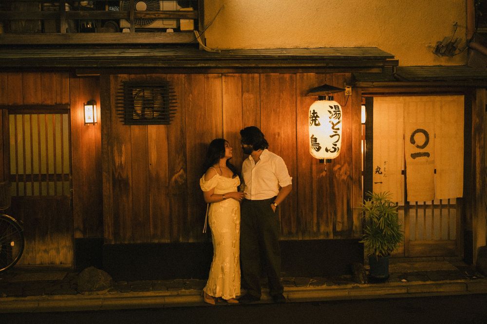 Couple sharing a kiss outside a traditional Japanese wooden building with a glowing paper lantern.