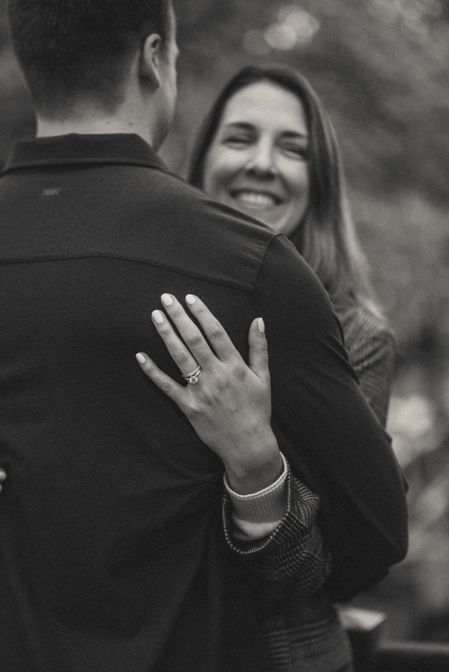 Close-up of engagement ring on woman’s hand as she embraces her fiancé, black and white Amsterdam setting.