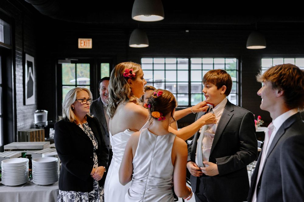 A black and white wedding reception photo showing guests mingling and socializing in an indoor venue.