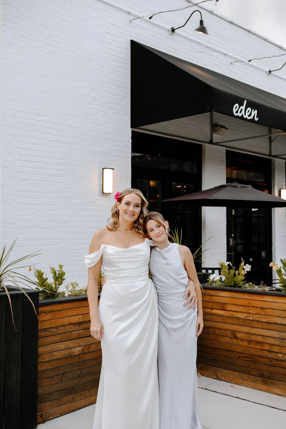 Wedding party poses outside modern venue with white walls and wooden planters.