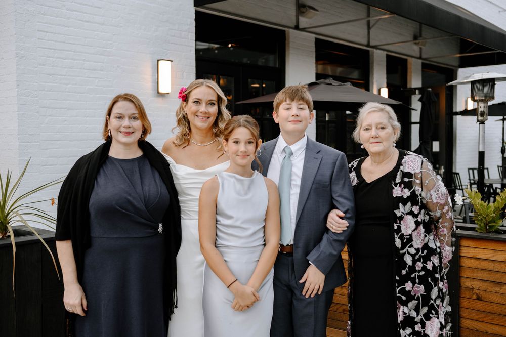 Wedding party members gather for candid moments at an outdoor venue with white brick walls and modern decor.