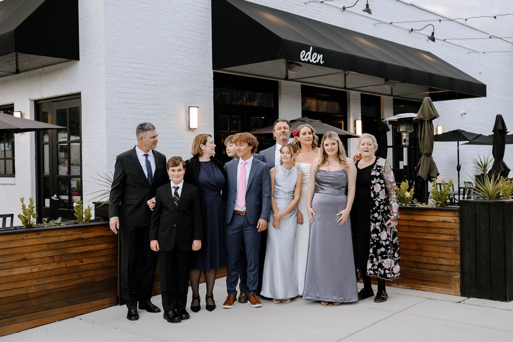 Wedding guests line up for formal photos outside modern venue entrance.