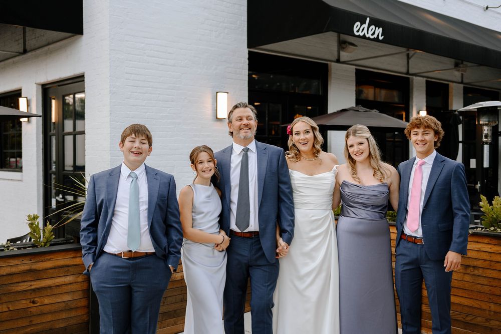 Group photo of wedding attendees lined up against a white building exterior.