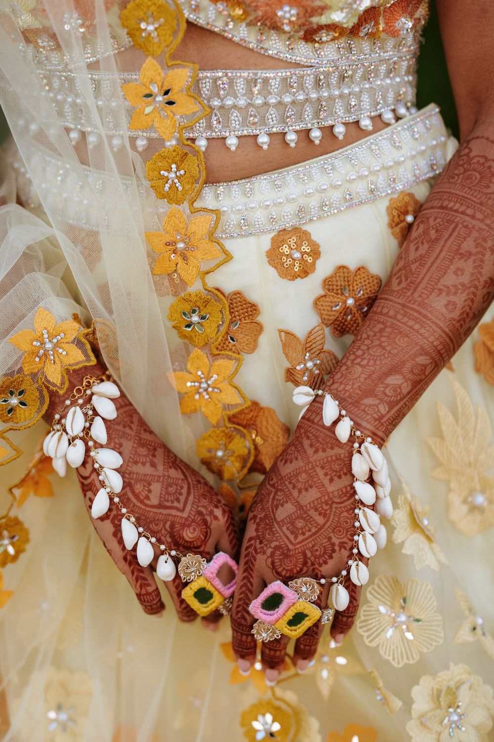Intricate henna designs adorn hands against a backdrop of white and gold floral embellished fabric.