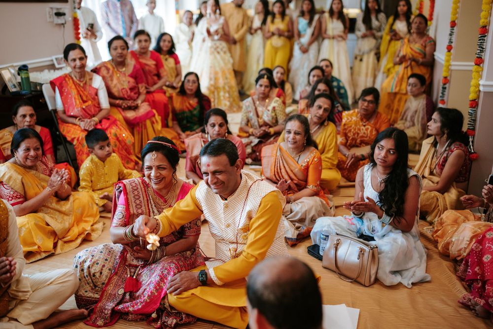 Traditional Indian wedding ceremony with guests seated on floor wearing colorful yellow and red attire during ritual.