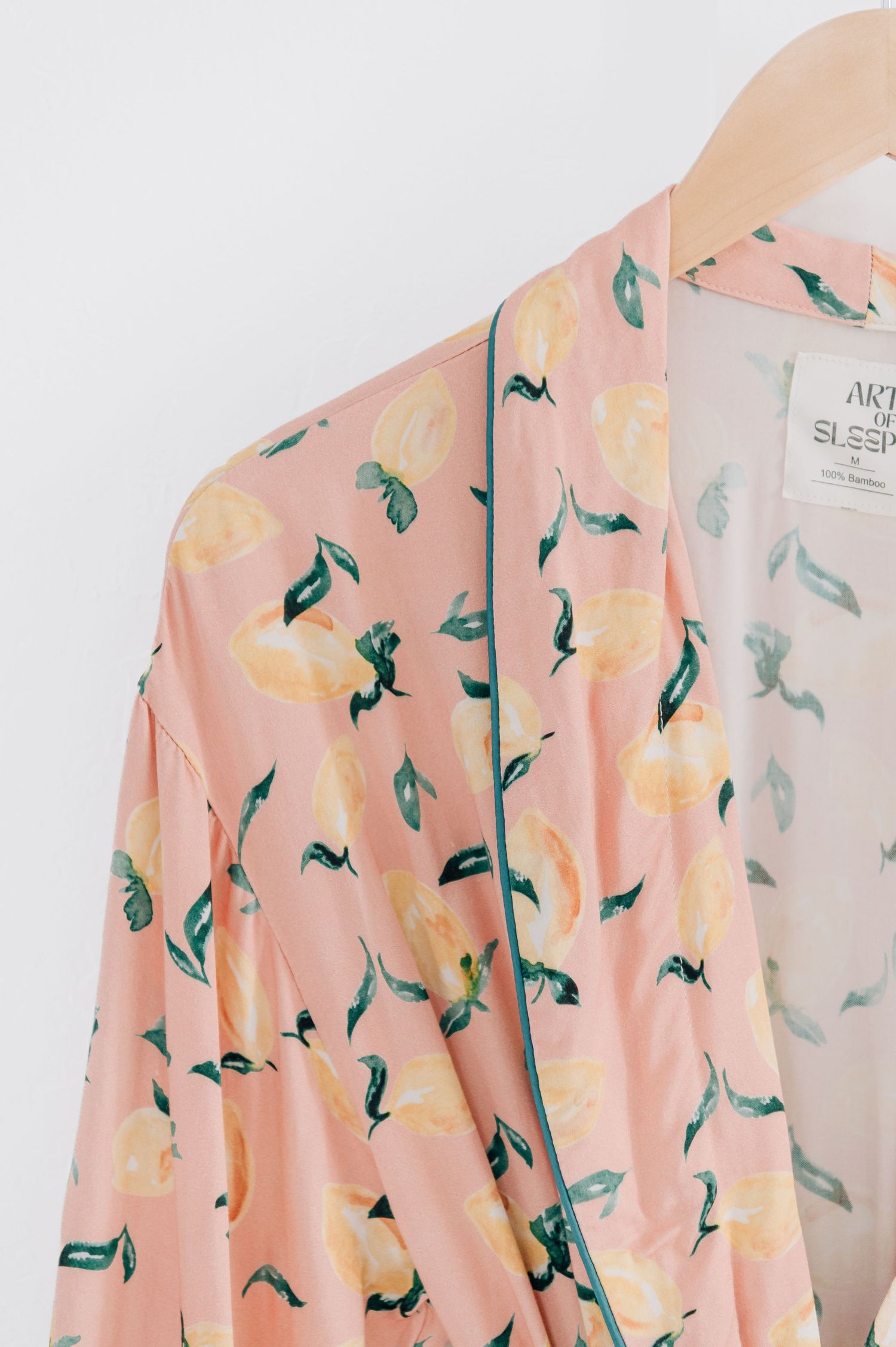 Pink floral kimono robe with yellow citrus fruit and green leaf print, hanging on a wooden hanger.