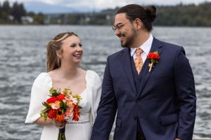 A couple shares a joyful moment by a lake on their wedding day, with mountains visible in the background.