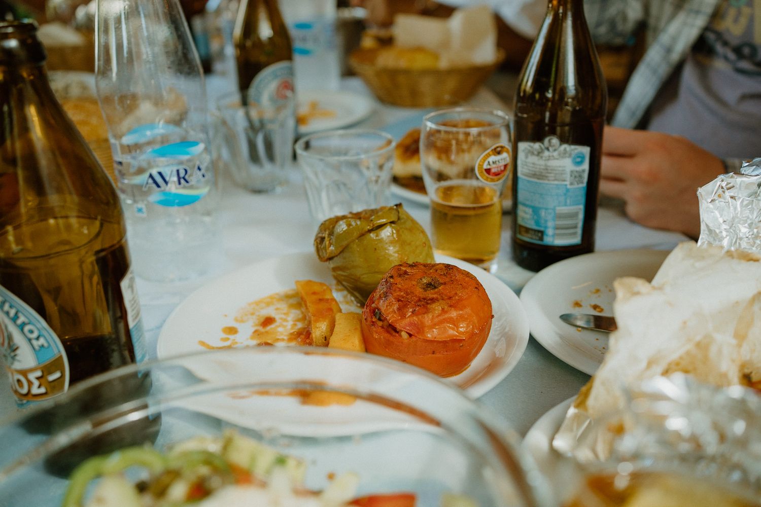 Vintage-style dining table setting with beer bottles, plates of food and glassware at a casual meal.