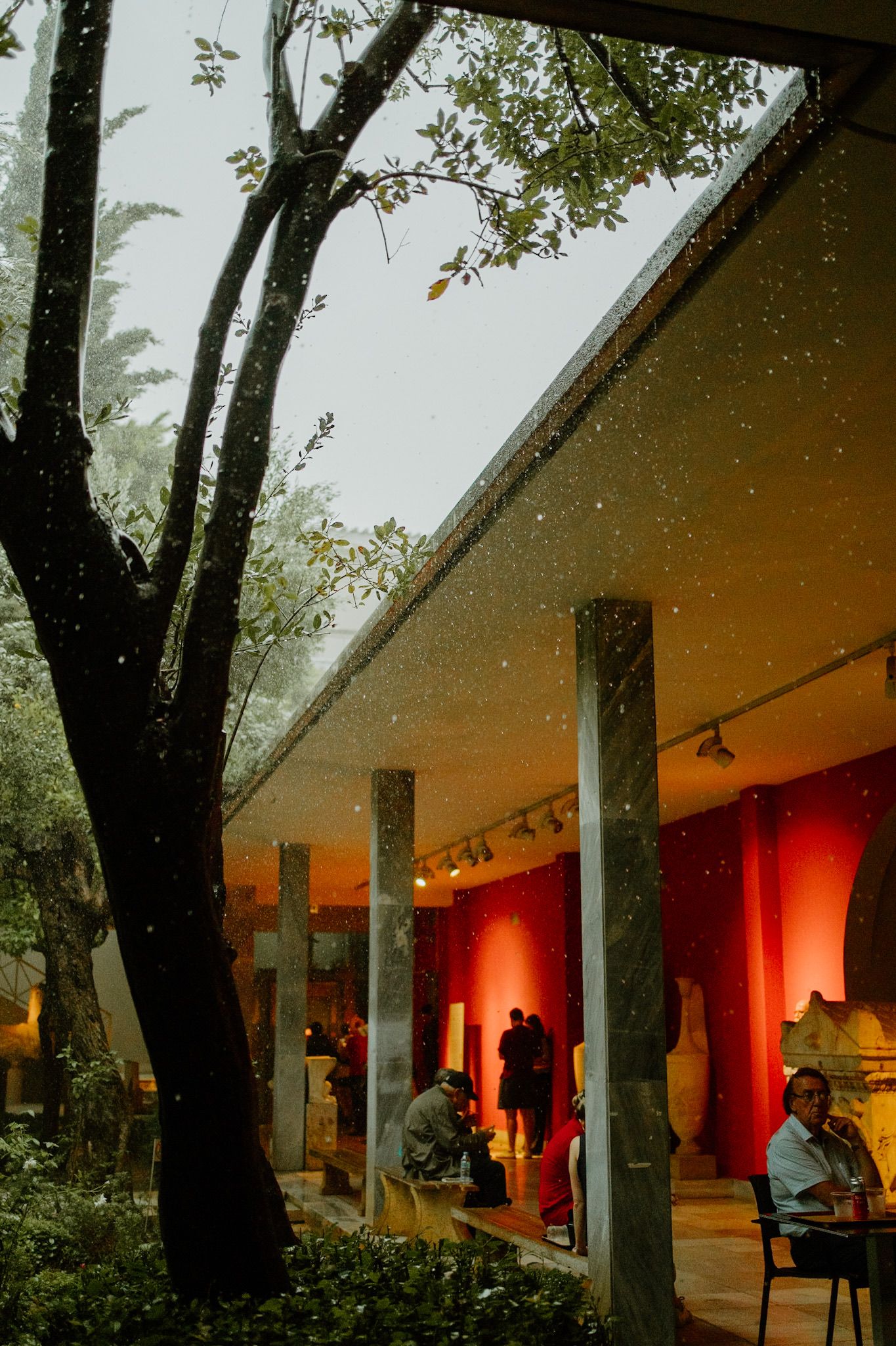 Covered outdoor patio with red-lit interior and silhouetted figures visible through glass windows at dusk.
