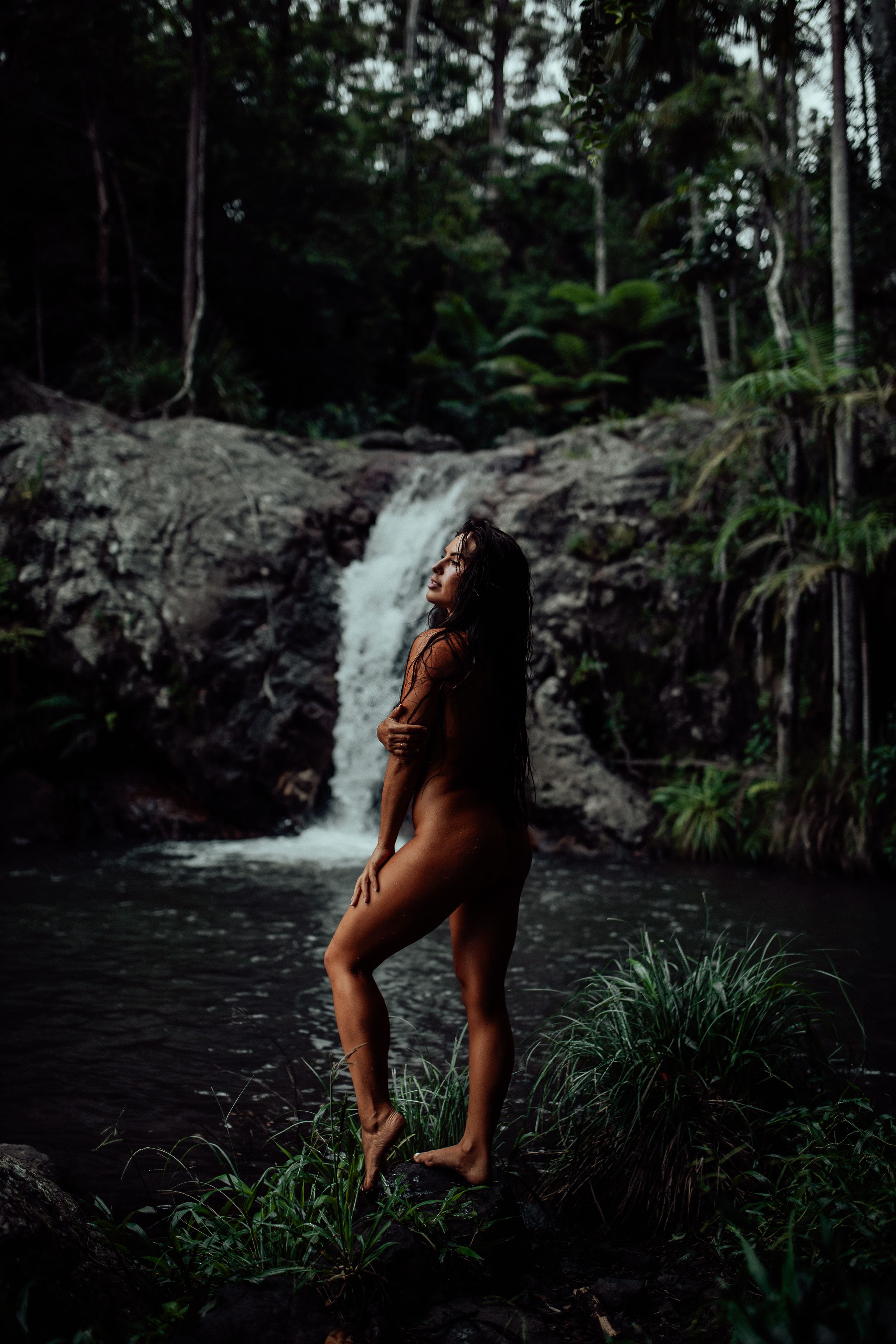 Silhouette against tropical waterfall in lush forest setting during golden hour.
