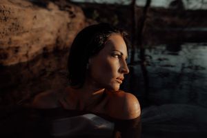 Moody outdoor portrait with golden sunlight casting glow on wet skin near water.