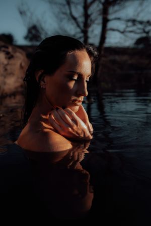 Artistic portrait in warm sunlight showing reflection in dark water with dramatic shadows.
