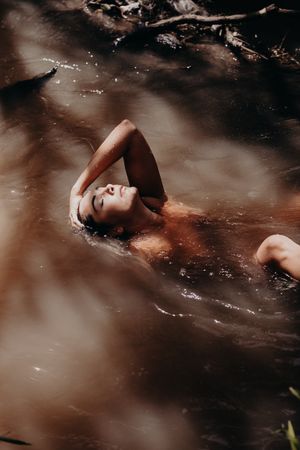 Atmospheric portrait of a person floating peacefully in dark forest waters.