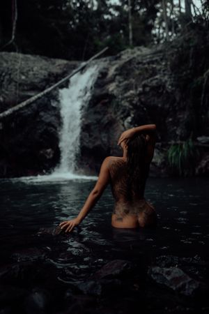 Silhouette of a person posing in dark waters with a waterfall backdrop.