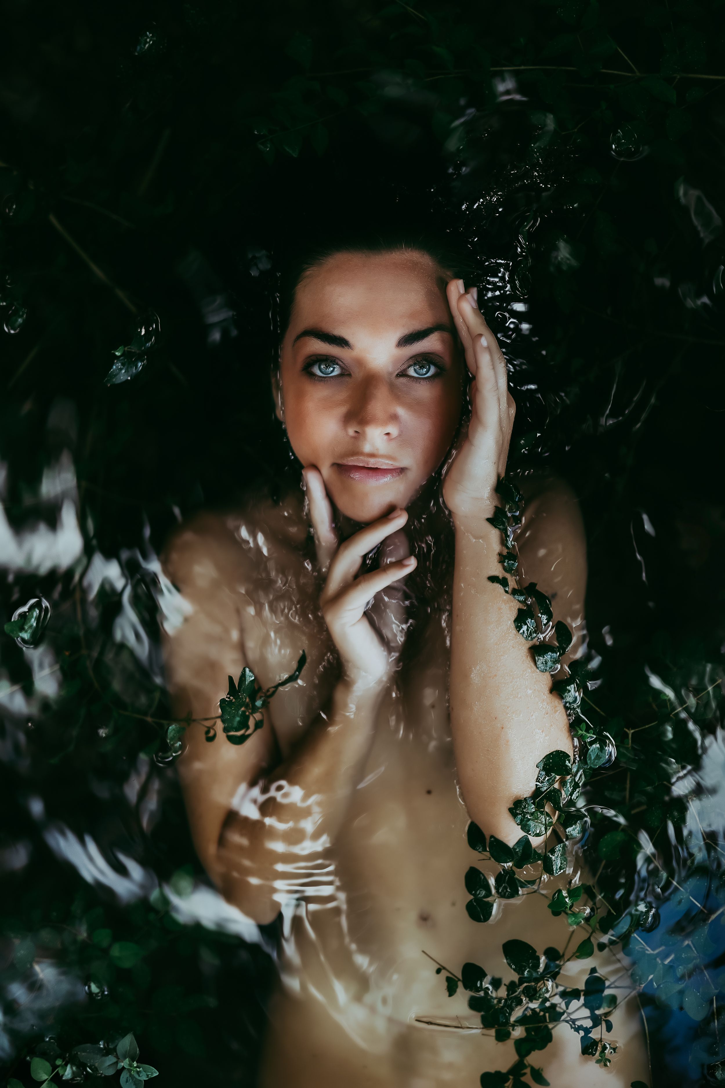 Ethereal portrait through leaves with dappled light creating natural patterns.