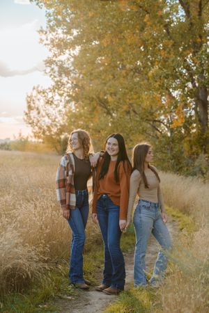 Three people in casual attire pose together on a path beneath golden autumn trees.