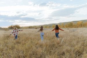 Three friends run joyfully through a golden prairie field on an autumn afternoon.