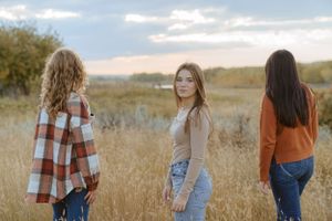 Three casual friends explore a prairie field together during autumn.
