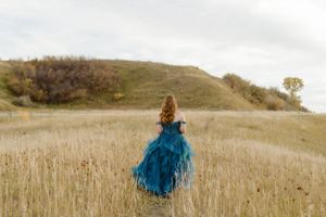 Person in flowing blue gown walks through golden grass on rolling hillside at MD Taber.