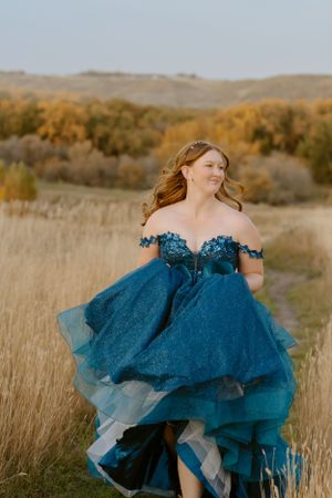 A stunning blue off-shoulder ballgown with sparkles and layers flows in the autumn prairie breeze.