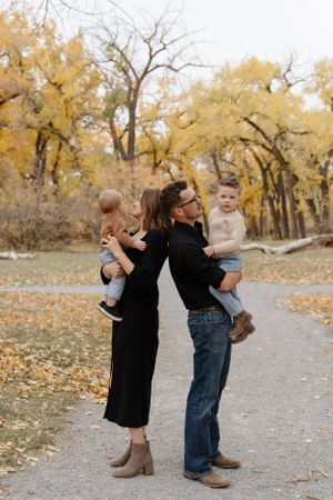 A family shares a playful moment on a path lined with golden autumn trees.