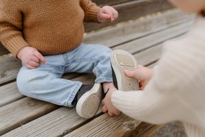 Close-up view of baby feet in light blue jeans and white canvas shoes on wooden deck.