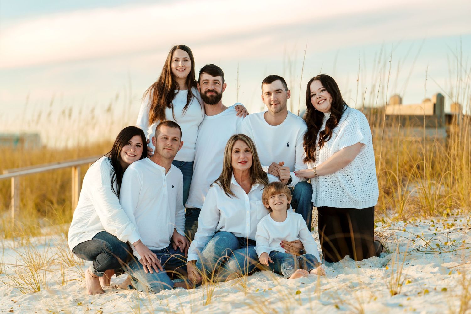 A group dressed in coordinating white and blue outfits poses together on a sandy beach at sunset.