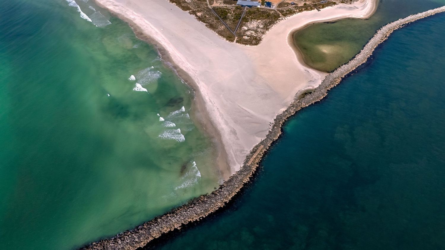 Aerial view of a sand spit with turquoise water on one side and dark blue ocean on the other.