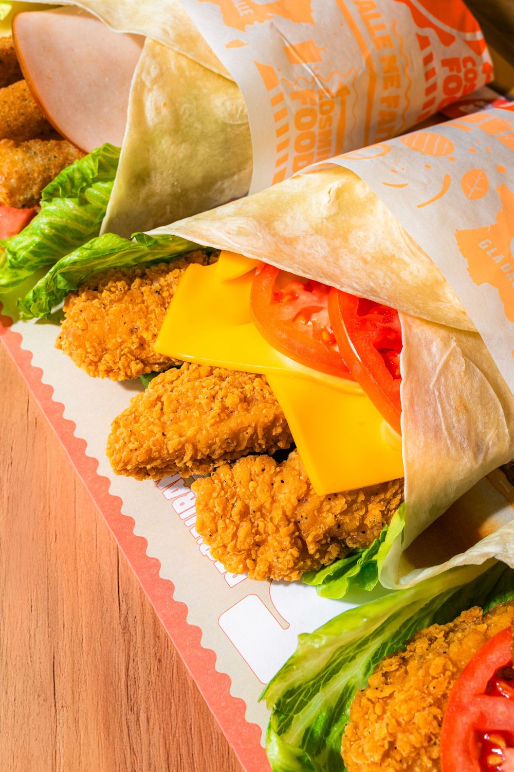 Fast food wrap filled with crispy fried chicken, lettuce, tomato and cheese on wooden surface.