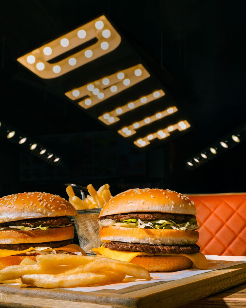 Gourmet burgers and fries on wooden board under decorative ceiling lights. Mtlshutter photography