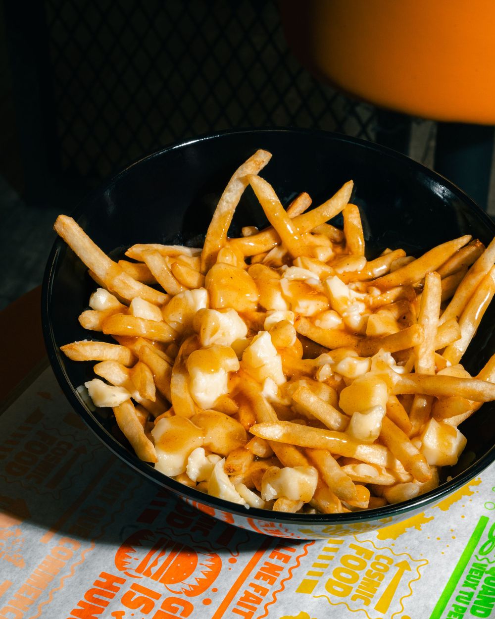 Golden french fries topped with melted cheese curds and gravy sauce in a black bowl. Mtlshutter photography