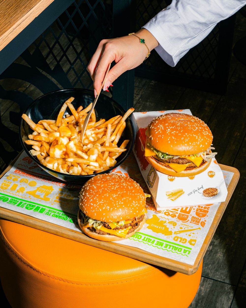 Cheeseburgers and poutine-style fries served on orange seating with branded paper wrapping. Mtlshutter photography