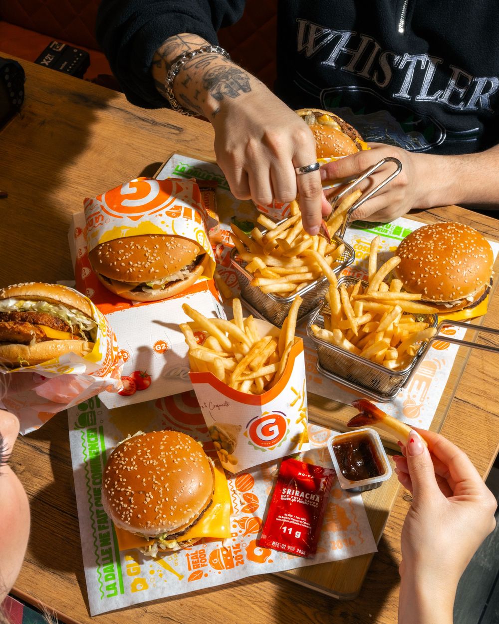 Multiple cheeseburgers and fries arranged on branded paper with sauce packets on wooden surface. Mtlshutter photography