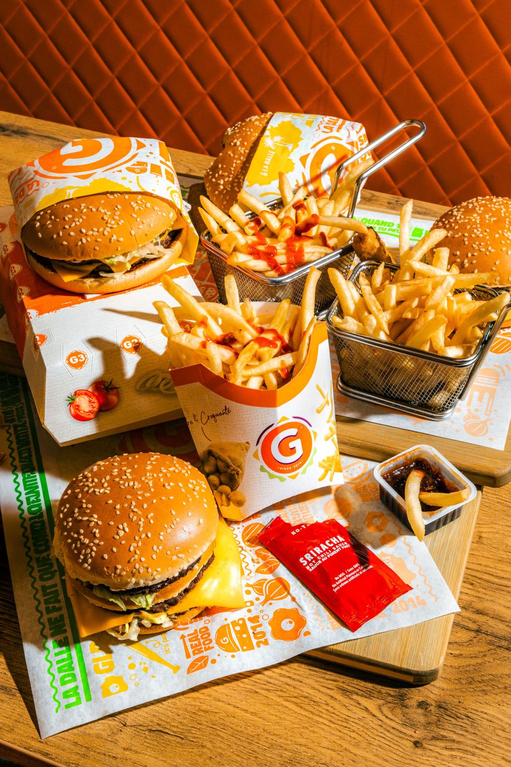 Fast food meal spread with cheeseburgers, french fries, and ketchup packets on a wooden table with orange background.Mtlshutter photography