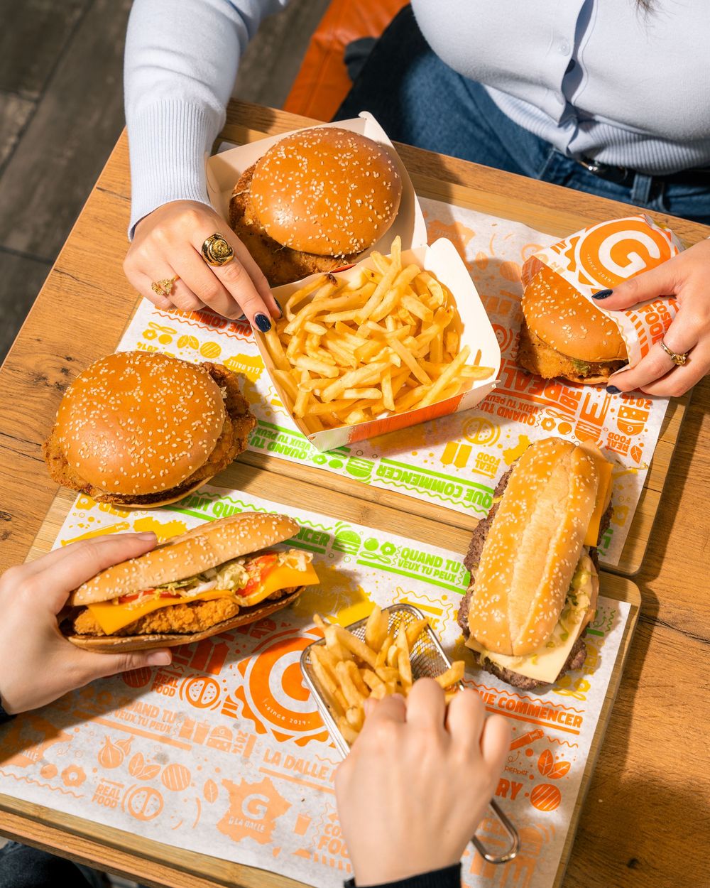 Someone enjoying a fast food burger and fries combo set from a takeaway restaurant on a wooden table.