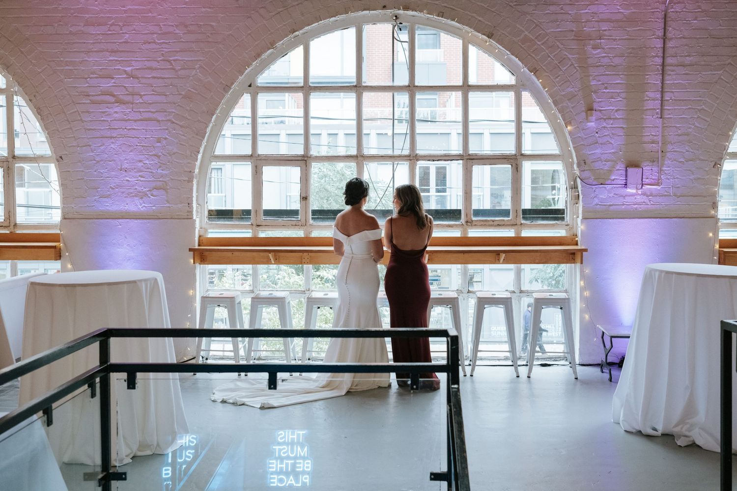Modern wedding venue with arched windows, white tables, and purple uplighting.