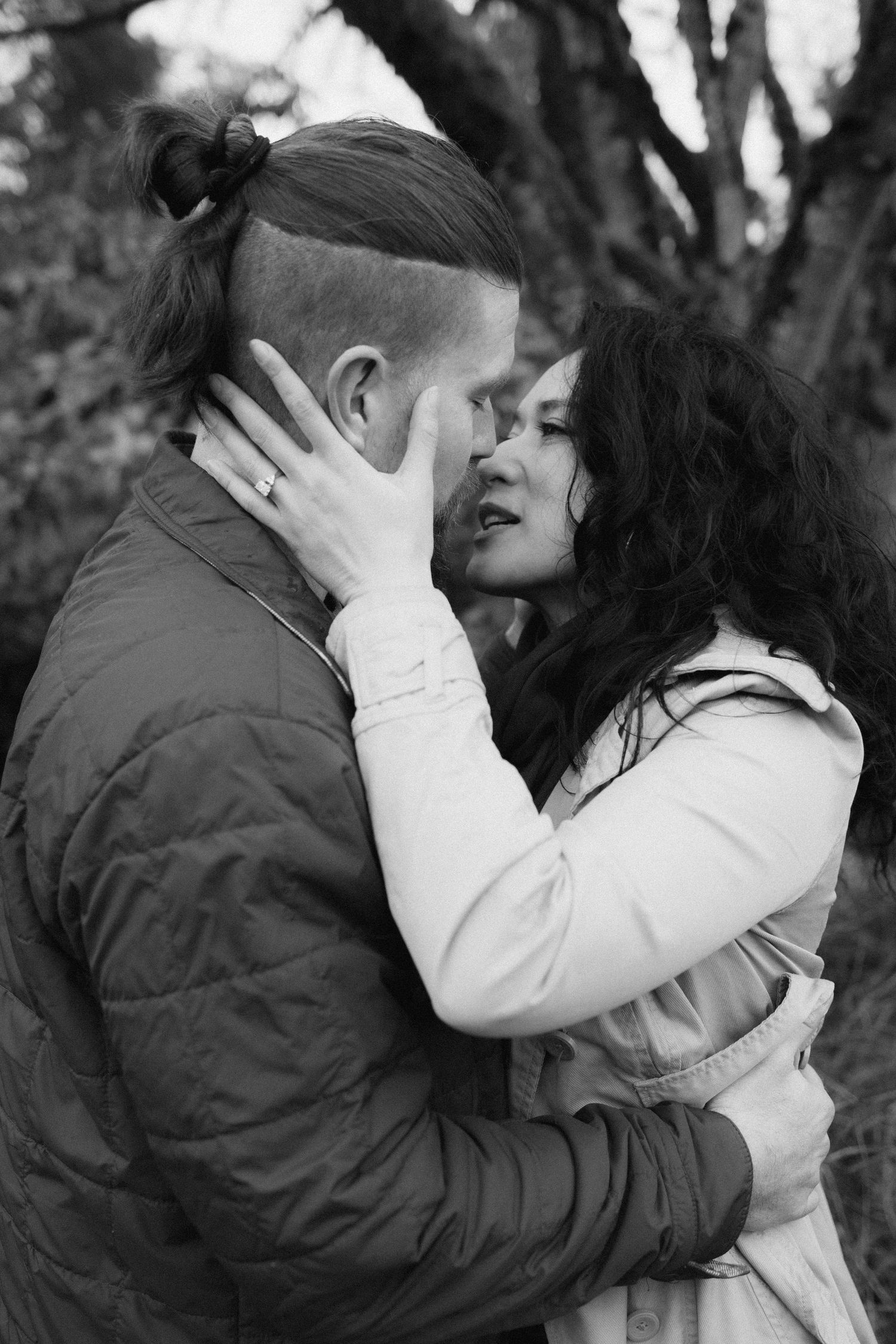 A romantic couple sharing an intimate moment outdoors in black and white photography.