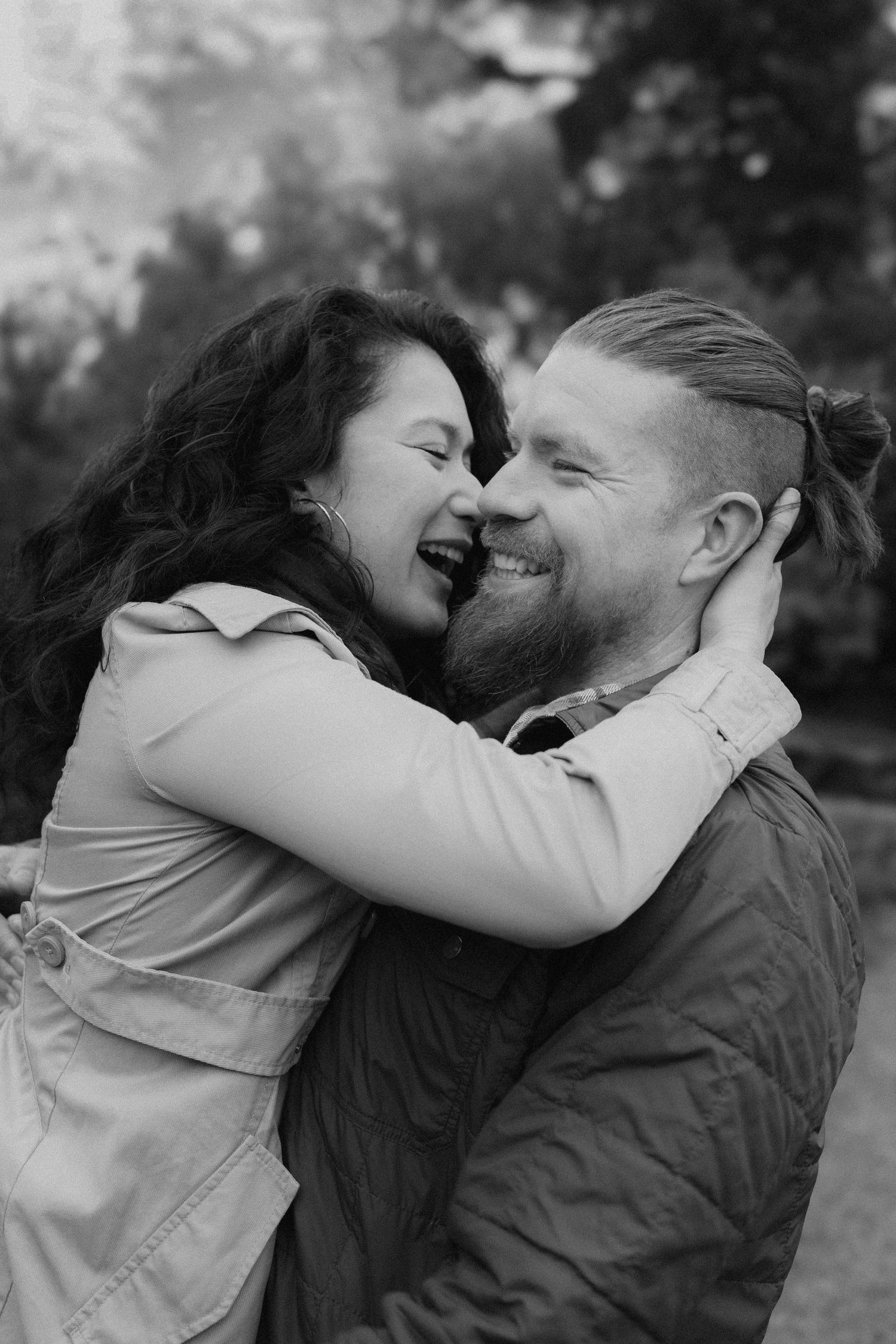 A candid black and white photo of a couple laughing and embracing outdoors.