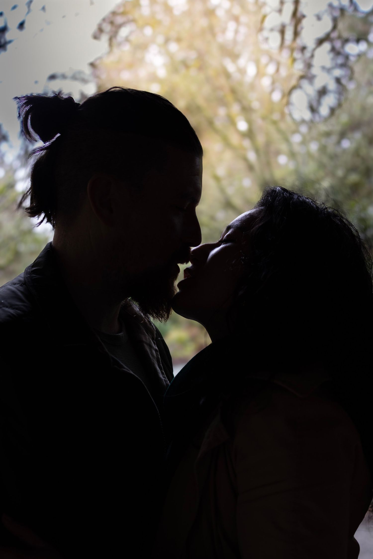 A silhouetted couple sharing an intimate moment against a backlit natural background.
