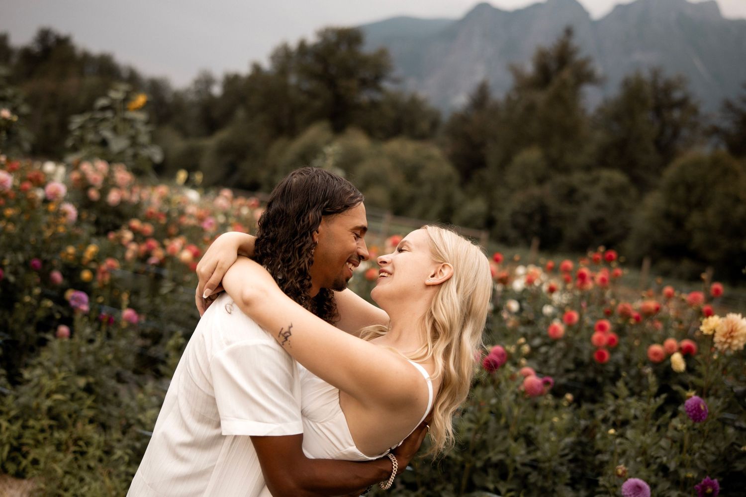 Couple embracing and almost kissing in a colorful flower garden with mountains in the background.