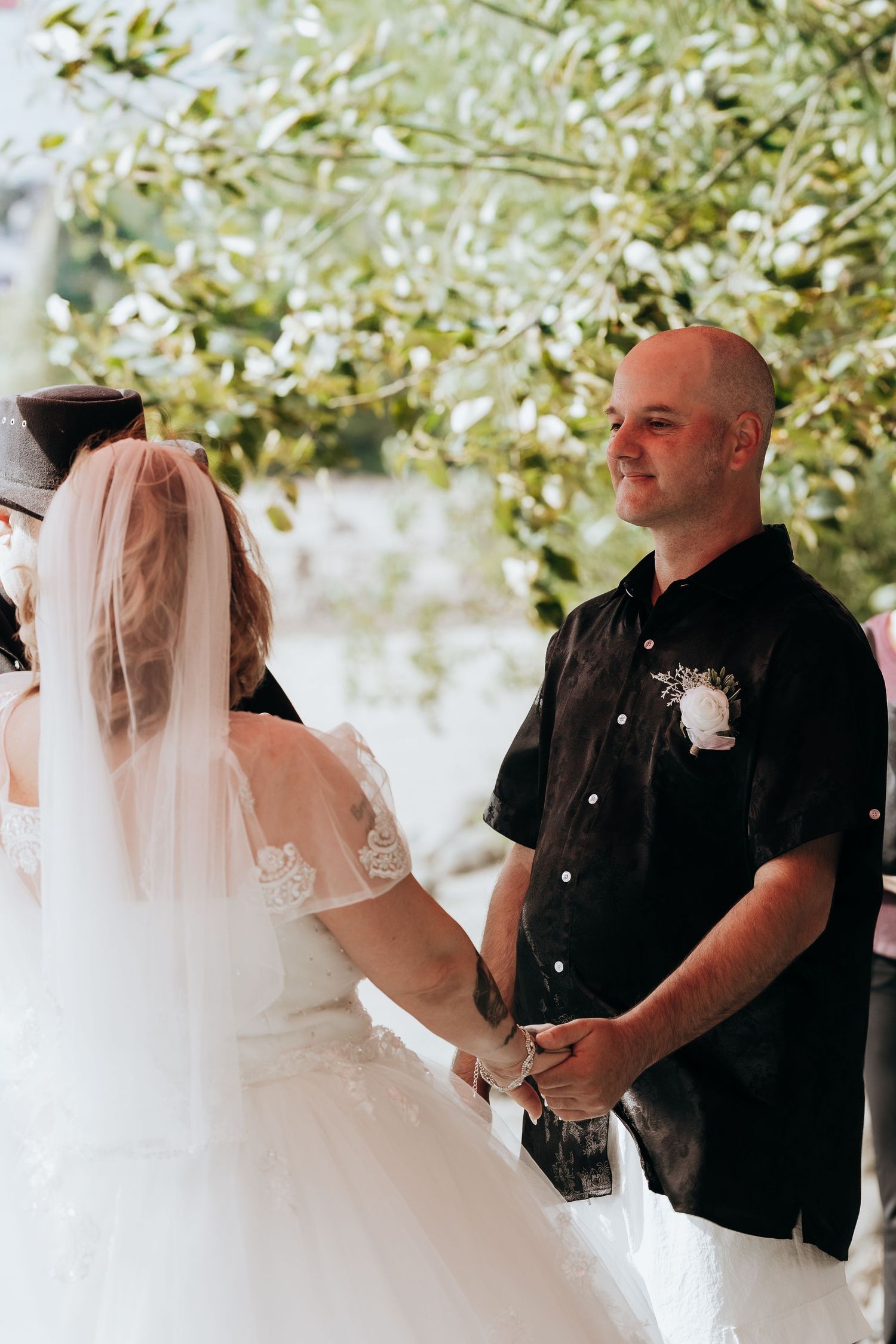 A romantic wedding ceremony moment under blooming tree branches with white florals and greenery.