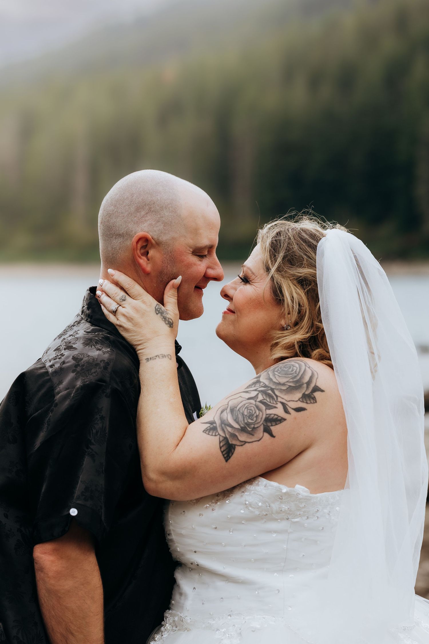 A romantic wedding moment captured by the lake with mountains and forest in the background.