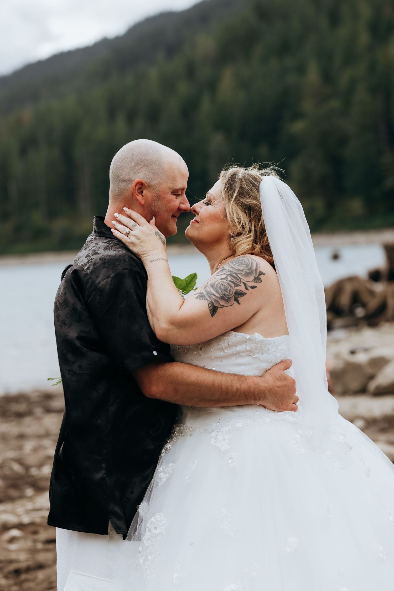 Romantic wedding couple embracing on a rocky beach with mountains in the background.