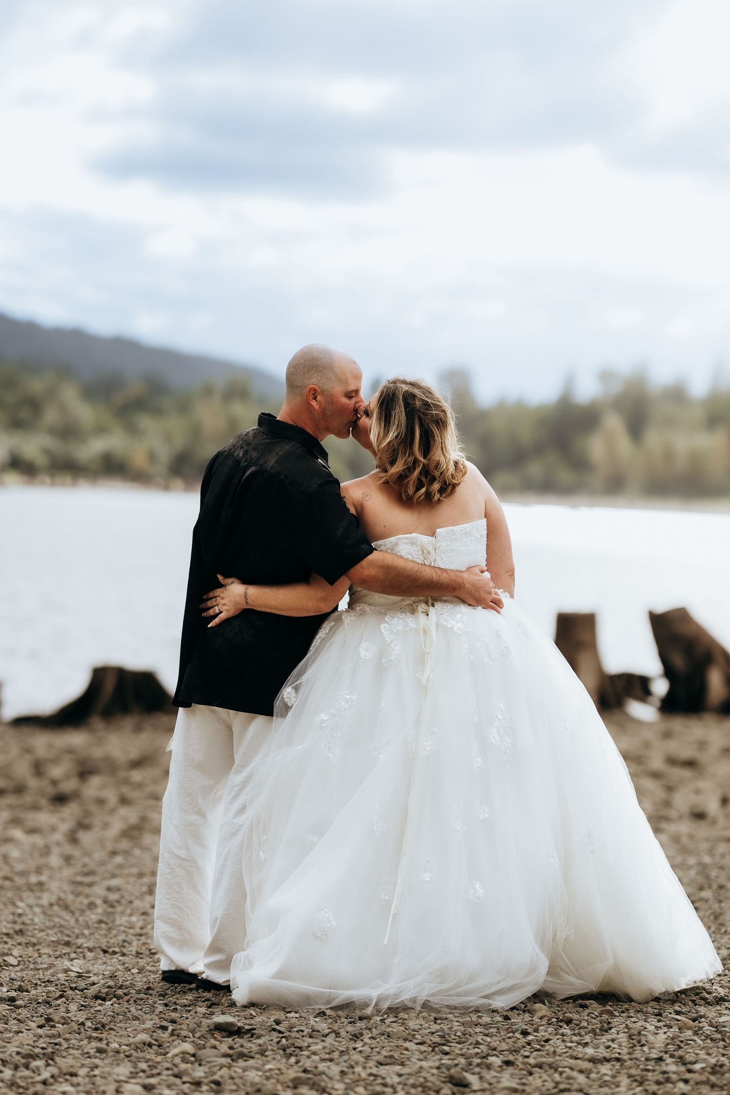 Newlyweds share intimate moments while sitting together on a rocky beach shore.
