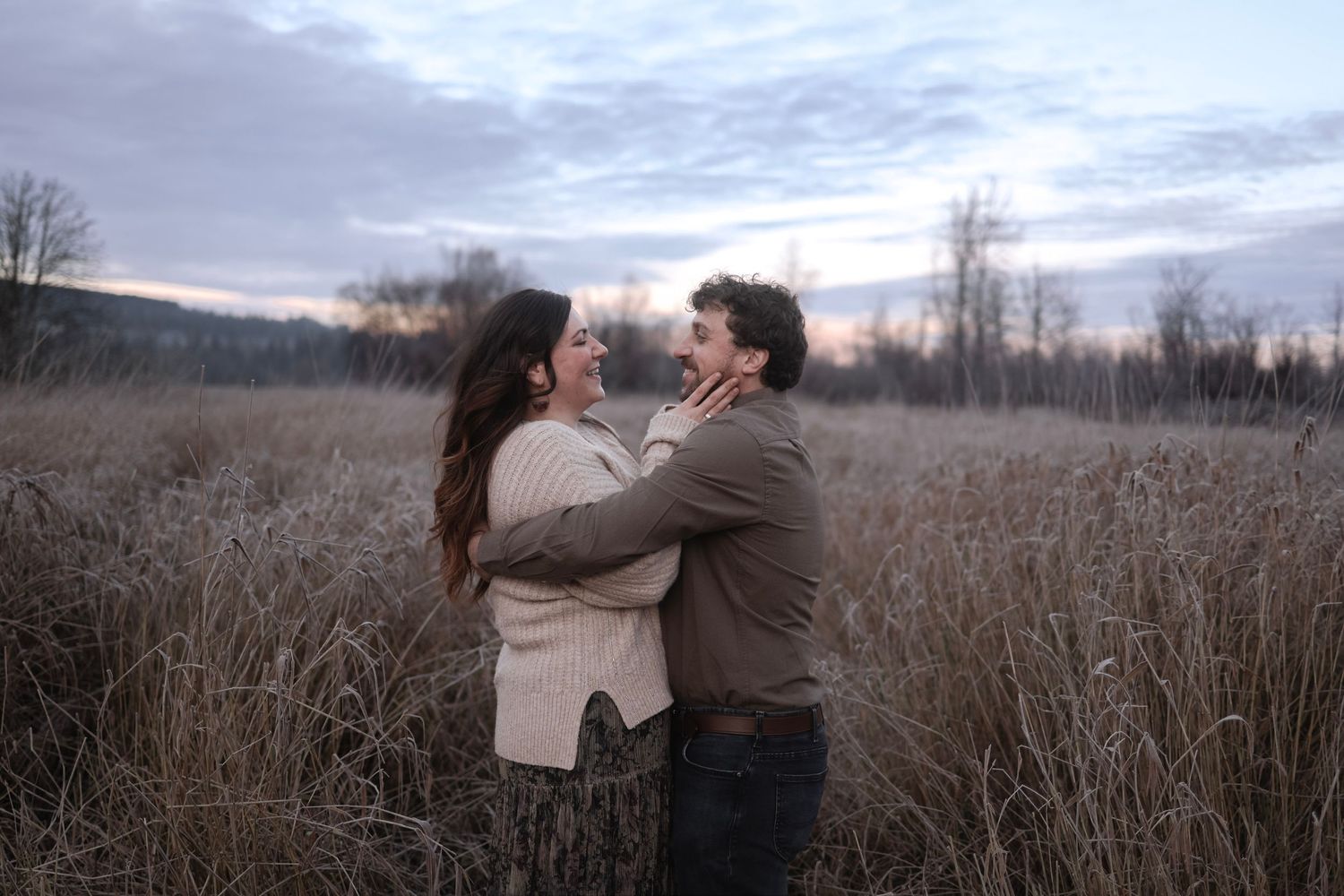 Couple embracing in a field of tall grass during sunset.